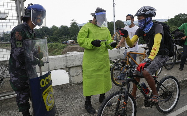 마닐라 외곽의 한 검문소에서 안면 보호대를 착용한 경찰이 자전거 여행객을 검사하고 있다. 사진=뉴시스