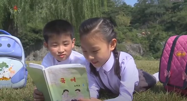 북한 어린이들이 잔디밭에 누워 소학교 국어책을 보고 있다. 사진=조선중앙TV
