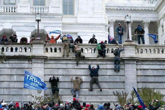 지난해 1월 6일 도널드 트럼프 미국 대통령의 극렬 지지자들이 워싱턴DC 국회의사당에 난입하기 위해 담벼락을 오르고 있다. 워싱턴=AP